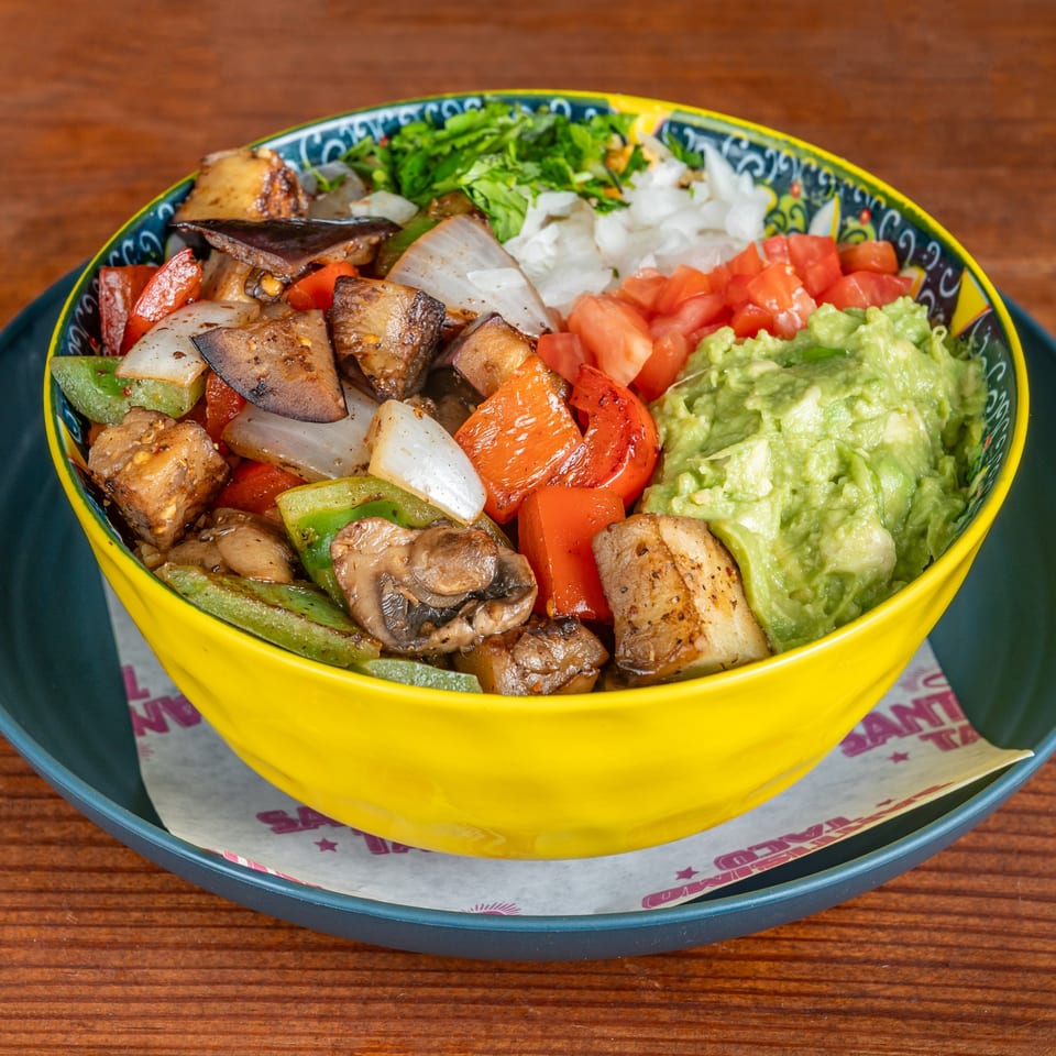 Colorful bowl of grilled chicken, vegetables, diced tomatoes, lettuce, and guacamole on a patterned plate.