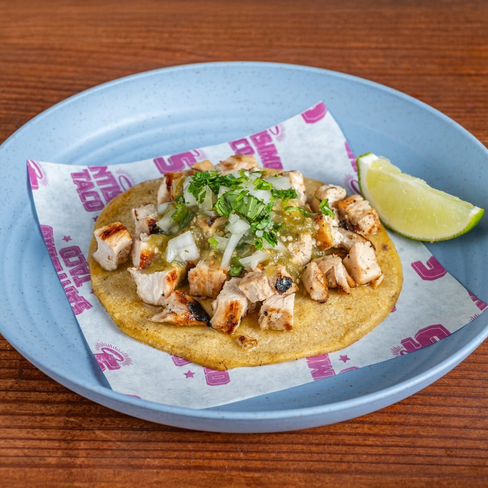 Grilled chicken tostada topped with green salsa, diced onion, and cilantro, served with a lime wedge on a blue plate.