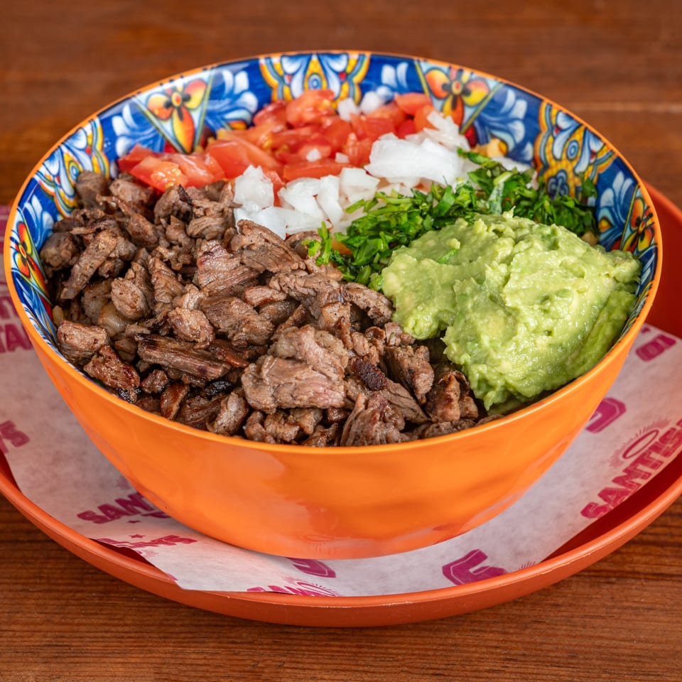 Colorful bowl of grilled beef topped with diced tomatoes, onions, cilantro, and guacamole on an orange tray.