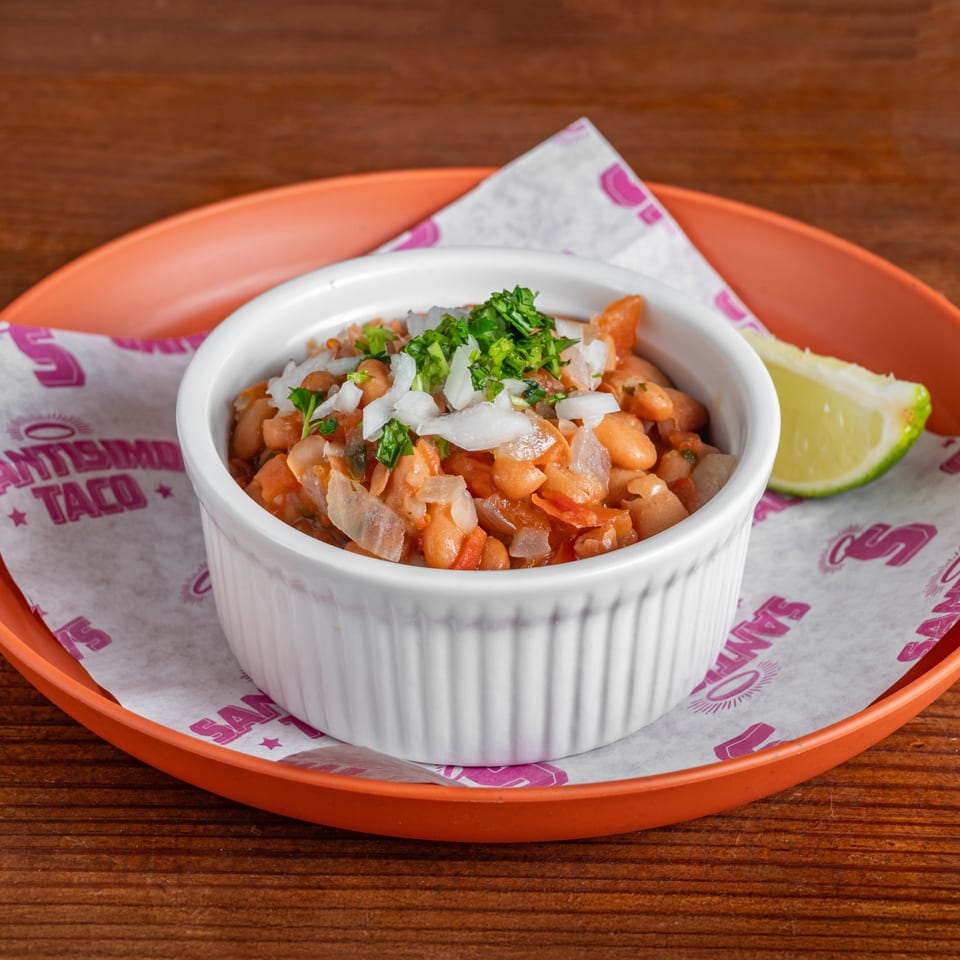 Bowl of seasoned pinto beans topped with chopped onions and cilantro, served with a lime wedge on an orange tray.