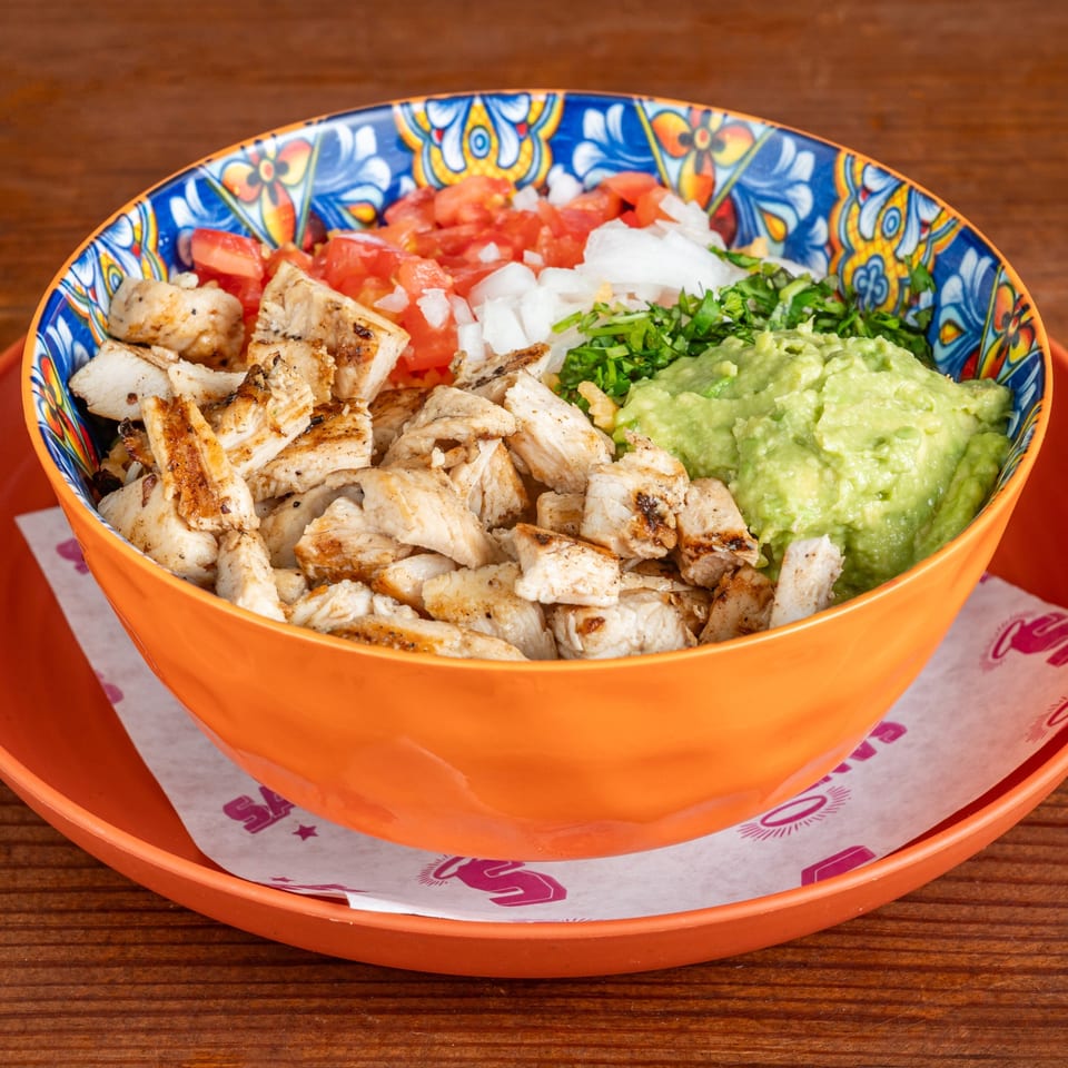 Bowl of grilled chicken topped with diced tomatoes, onions, cilantro, and guacamole on an orange restaurant tray.
